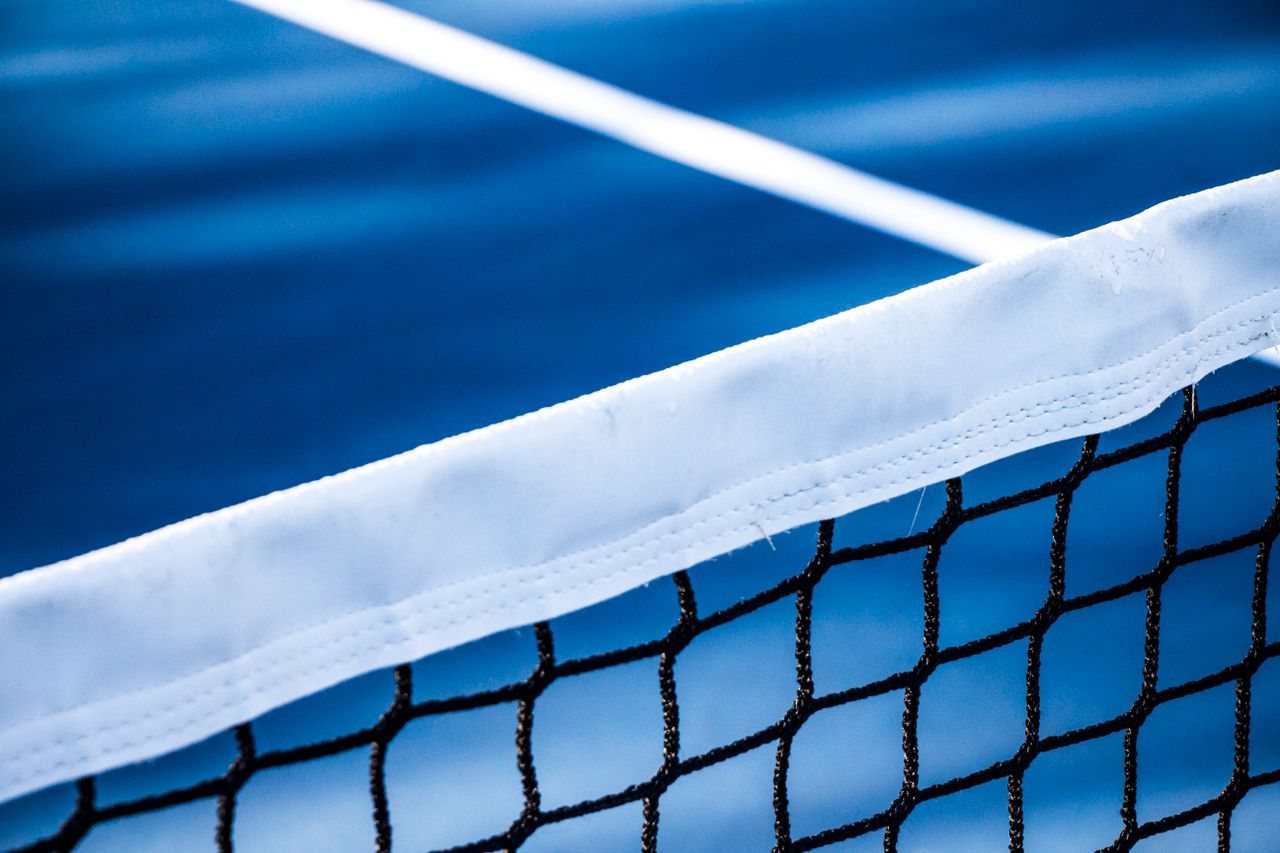 Sharp close-up of a tennis net with a blue court in the background, perfect for sports-themed designs.