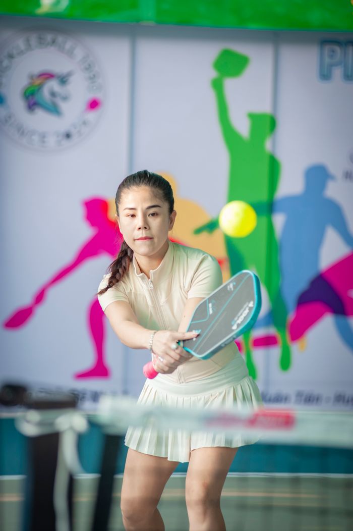 about-us-01 Focused Asian woman playing indoor pickleball with colorful background in Hanoi, Vietnam